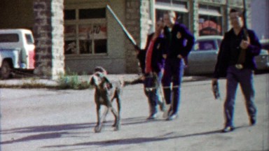 1959: Boys carry guns walking dog in parade on main street downtown.