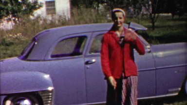 1958: Confident woman fashion red coat blue classic car stroll.