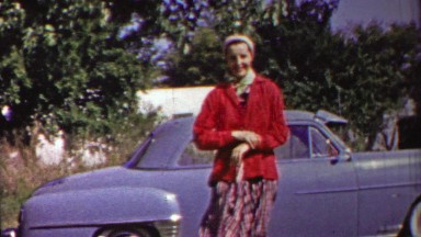 1958: Woman sitting down front yard play black dog blue car.