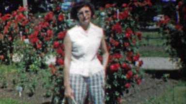 1961: Annoyed Woman Begrudgingly Poses in Red Rose Bushes