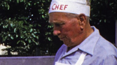 1964: Manly big chef hat outdoor cook grilling meat.