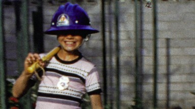 1964: Middle school aged salutes military march fireman hat costume.