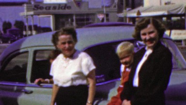 1964: Family gathering roadside seaside service station classic car.