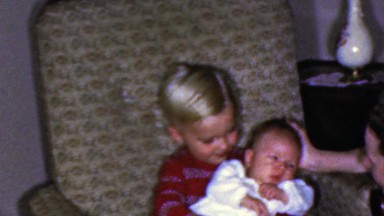 1961: Cute boy holding baby brother blows kisses camera.