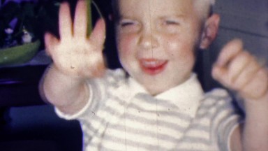 1961: Cute caucasian boy blows kisses waves birthday cake candles.