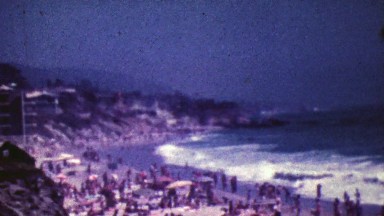 1964: Crowded tourist sunny ocean beach big waves crash on shore.
