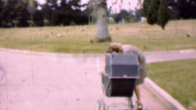 1957: Mother prepares baby stroller in tropical cemetery park.