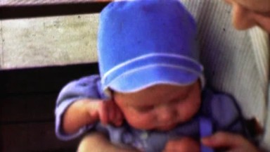 1957: Newborn baby boy in blue bonnet hat trying to get comfortable.