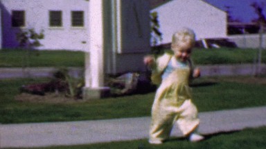 1957: Toddler looks drunk practices walking in suburban summer grass.
