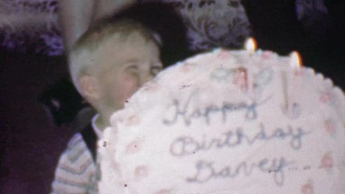 1957: Happy birthday Davey cake closeup blonde smiling child.