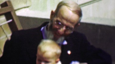 1958: Sharply dressed old grey bearded grandpa holds baby boy.