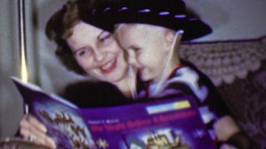 1957: Mother cowboy hat toddler boy read Christmas bedtime book.