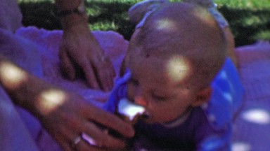 1957: Newborn baby eating ice cream cone summer picnic blanket.