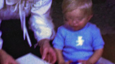 1958: Baby underwhelmed at crab food bib gift that mom unwraps.