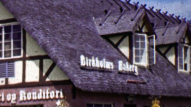 1962: Birkholm's Bakery shaker roof building Danish USA flags.