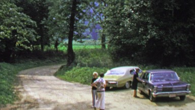 1974: Countryside parking lot classic cars gravel road spring green.