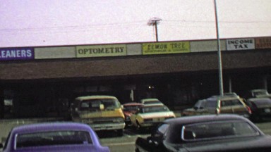 1974: Strip mall parking lot business storefront signs and logos.