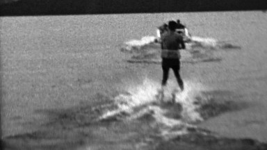 1962: Waterski man pulled behind speedboat dark mysterious lake.