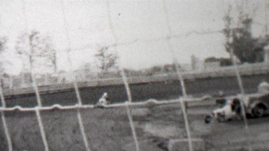 1939: Race track cars go kart racing behind thin wire safety fence.