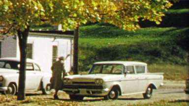 1967: Older woman enters passenger side of car waiting for driver.