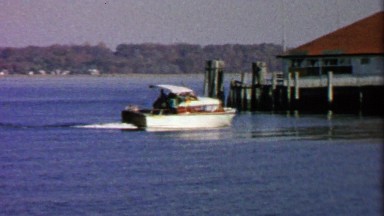 1967: Fancy powerboat docking on autumn lake boathouse.