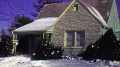 1964: Quaint brick facade bungalow suburban house garage driveway pan.