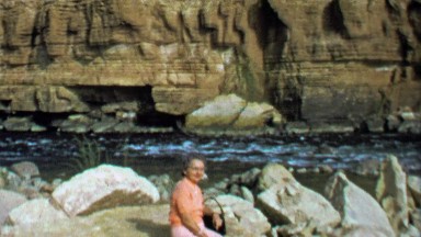 1964: Woman sitting on rock near wild western USA canyon river.
