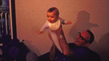 1961: Dad bouncing newborn baby boy in family room home.
