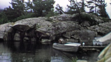 1961: Boat Docked on Wooden Pier by Rocky Landscape Hidden Cove