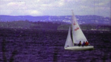 1961: Small white sailboat moving quickly across dark blue waters.