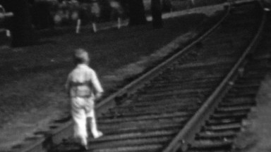 1957: Baby wildly running on railroad ties train tracks.