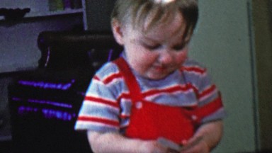 1957: Baby playing poker cards holds hand confused about betting.