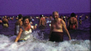 1952: Elderly couple play on crowded beach on hot summer day.