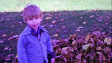 1967: Blue eyed kid with bowl haircut playing in autumn fallen leaves.