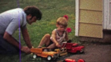 1968: Dad and Son Playing with Toy Model Dump and Fire Trucks in Backyard