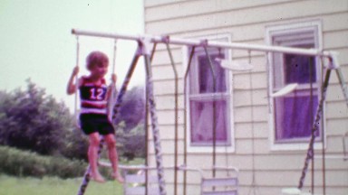 1968: Daredevil boy swinging on playground using hanging pull up bar.