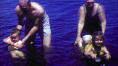 1952: Grandparents playing with kids in lake water vacation beach.