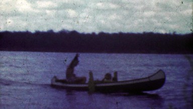 1953: Crafty man driving outboard motor rigged canoe across lake.