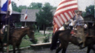 1955: Horse riding cowboys carry flags while folks watch the rodeo.