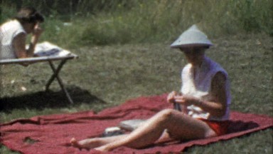 1954: Woman sunbathing on cut grass lawn in funny Asian style hat.