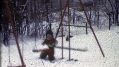 1953: Boy attempts to play on winter snow covered swing set playground.
