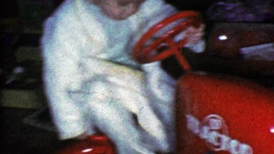 1953: Robed toddler boy riding red toy tractor Christmas morning.