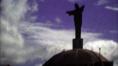 1975: Religious Jesus Statue atop Mountain Silhouette Passing Clouds.