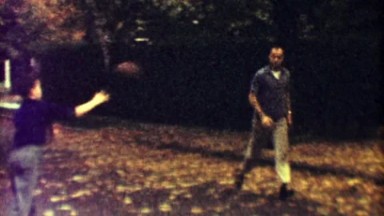 1963: Dad and son practice american football on autumn suburban street.