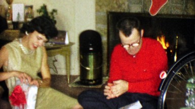 1963: Parents opening holiday Christmas gifts roaring yuletide fireplace.