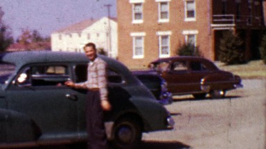 1955: Man making funny face about to enter classic car parked.