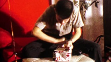 1964: Boy unwraps fishing reel Christmas gift.