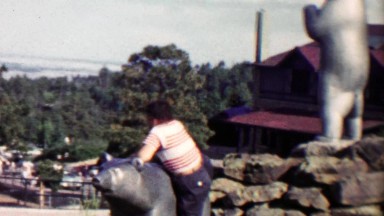 1959: Boy has trouble climbing bear statue mom helps.