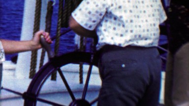 1961: Boy having trouble steering captains ship wheel mom helps.
