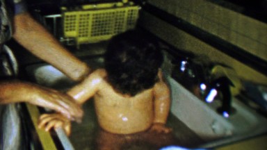 1961: Mother washing baby boy in home kitchen sink.